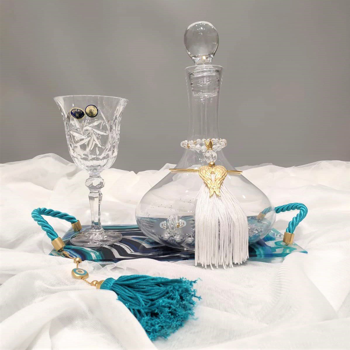 Σετ κουμπάρου σε κρύσταλλο Βοημίας με επίχρυσο στολισμό Tresento. Το σετ περιλαμβάνει περίτεχνο δίσκο με σμάλτο και πλεξιγκλάς, ιδιαίτερη μποτίλια κρασιού και ποτήρι από κρύσταλλο Βοημίας, διακοσμημένο με επιχρυσωμένο 24 καρατίων στολίδι Tresento με φτερά αγγέλου, με πέταλο, γαλάζια φούντα και μεταξωτό κορδόνι. Όλα είναι χειροποίητα και κατασκευασμένα στην Ελλάδα.